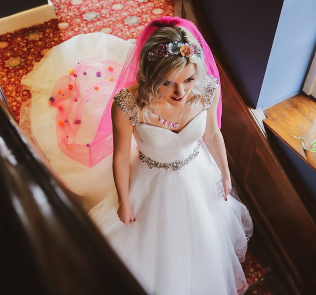 Bride wearing a coloured floral headpiece and pink veil on stairs in wedding venue.