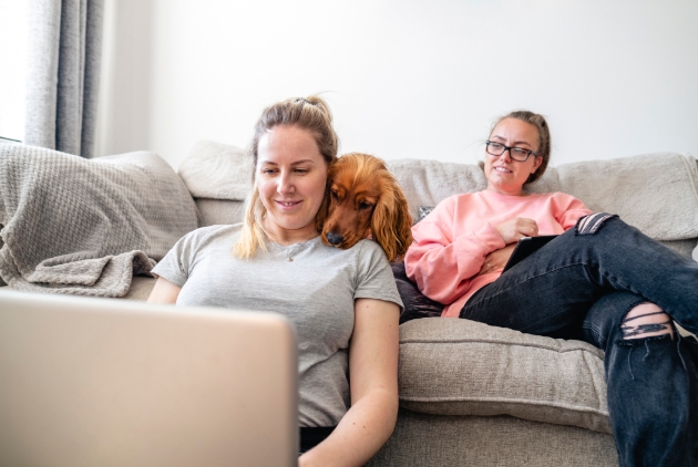 couple, one on sofa one sat on floor looking at laptop