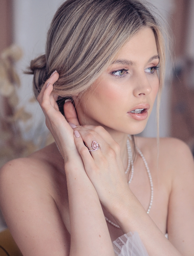 Blonde woman wearing a pink engagement ring and pearl necklace.