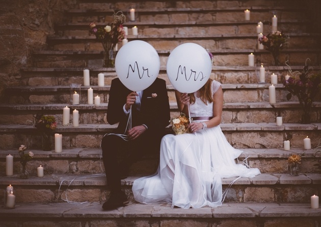 Newlywed couple sitting on steps with candles and flowers holding Mr and Mrs balloons