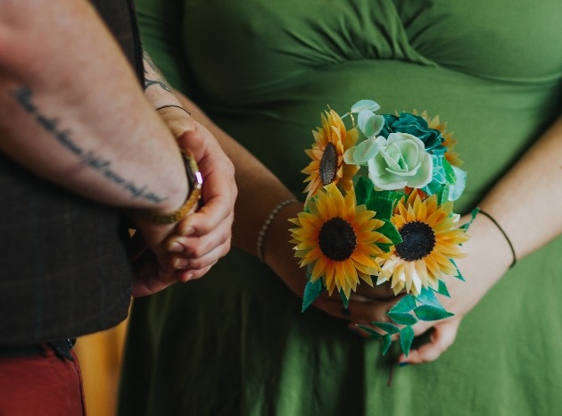 Bridesmaids in green dress holding recycled plastic bouquet with sunflowers.