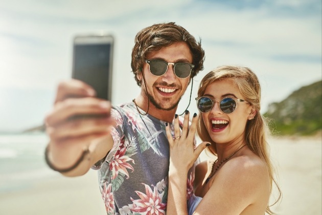 couple in sunglasses taking a selfie of engagement ring 