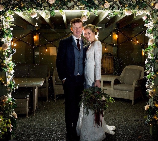 Wedding couple stood in floral archway.