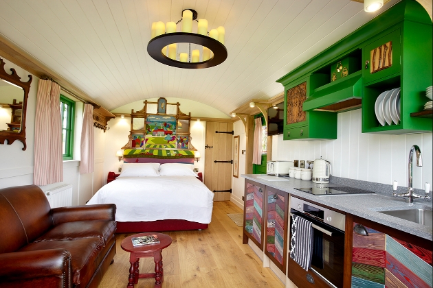 inside shepherd hut which has a leather sofa and brightly coloured folk-style kitchen cupboards and a large bed