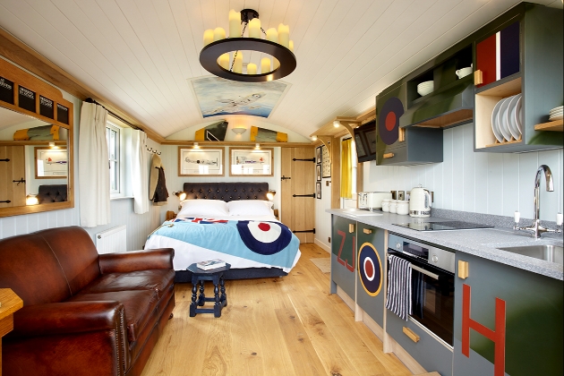 Inside shepherd hut which has a leather sofa and is themed with aeroplane decor