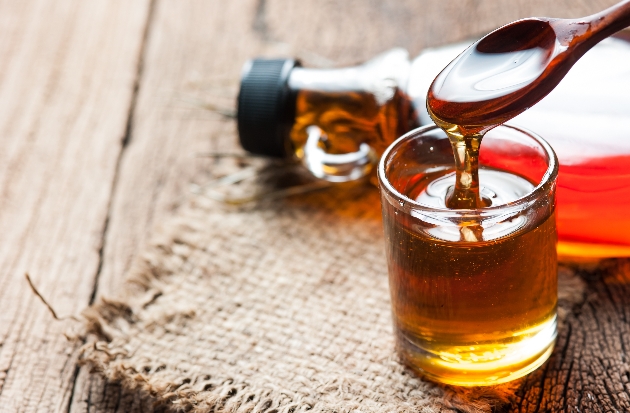 maple syrup pouring from a wooden spoon into a glass