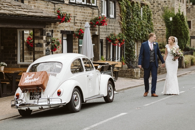 Couple exiting wedding venue with a VW Beetle outside