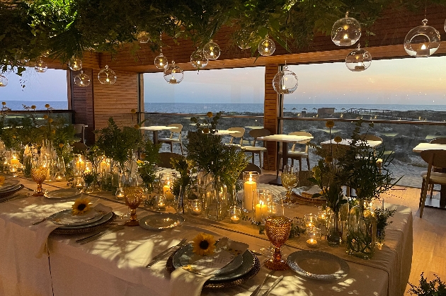 tables at night with candle light baubles hanging from foliage on the ceiling with long tables and sea views