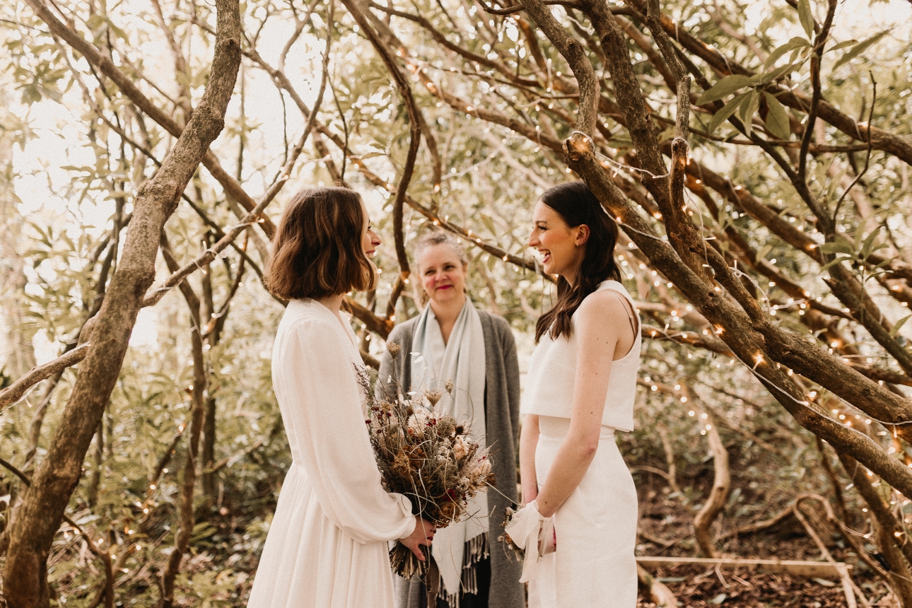 couple in wedding dress standing in the woods with a registrar