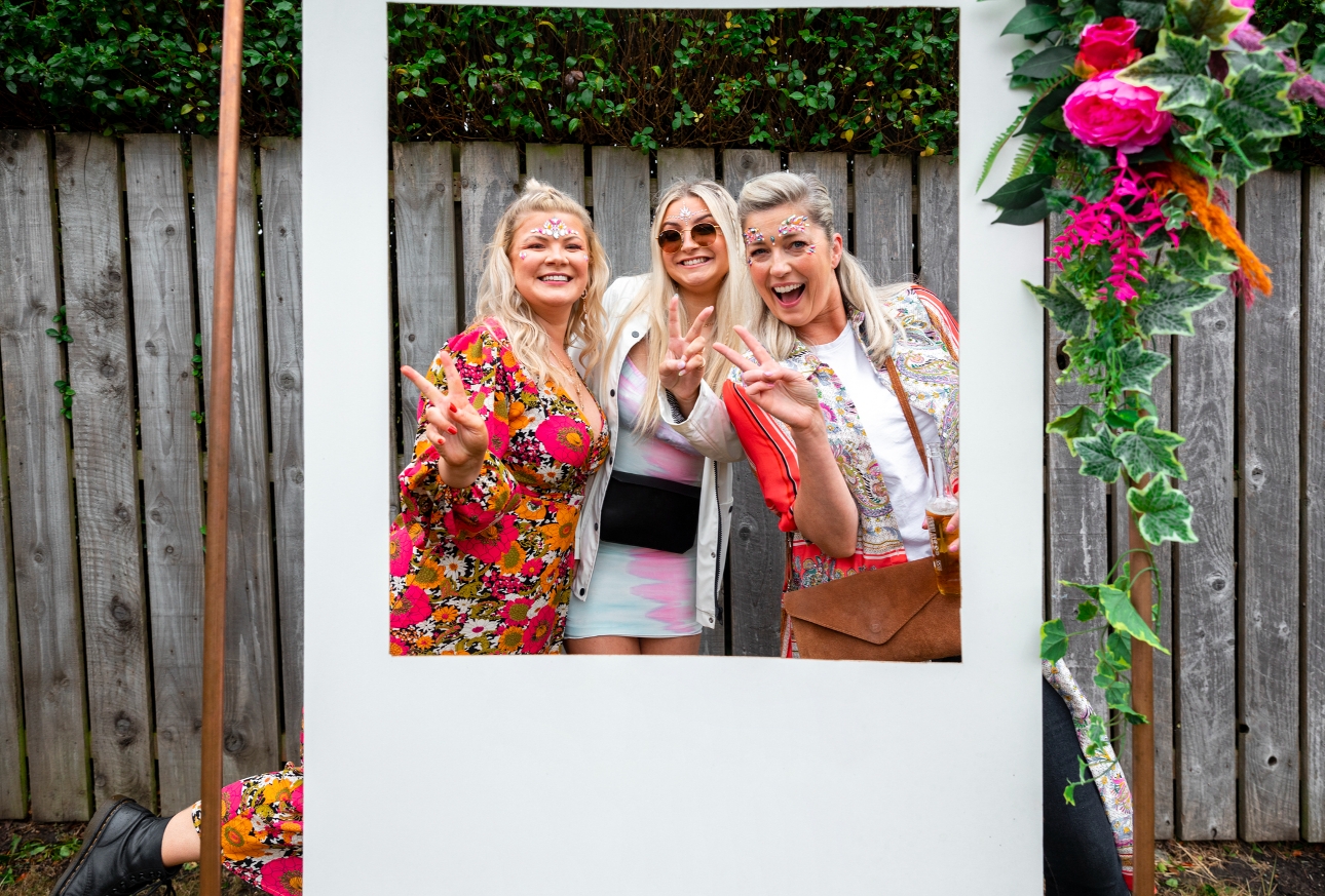 three women in festival gig clothes posing behind a Polaroid cut out photo booth