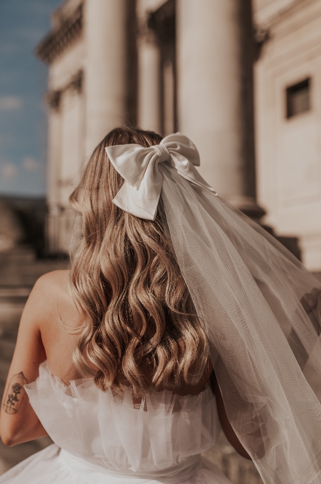 brides hair with a veil in it featuring a white bow clipped in