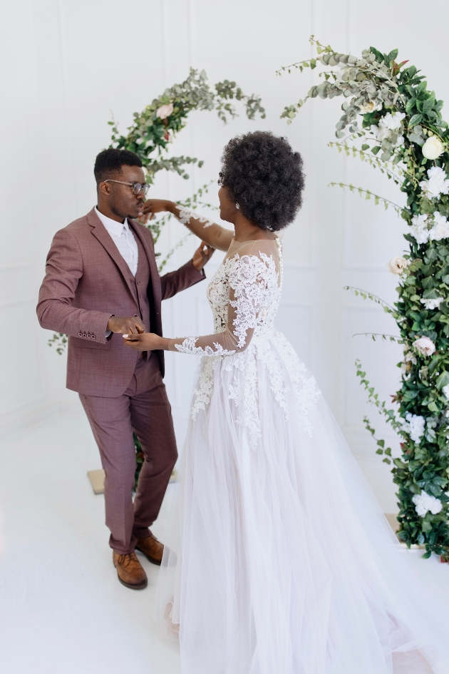 bride in a dress groom in red suit, dancing in front of a floral arch