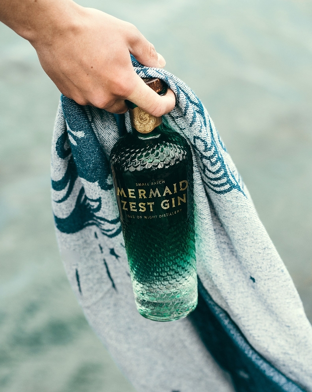 blue bottle with gold writing held in a hand with a beach towel