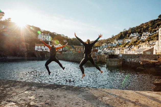 three friends in wet suits jumping in to the sea in Cornwall