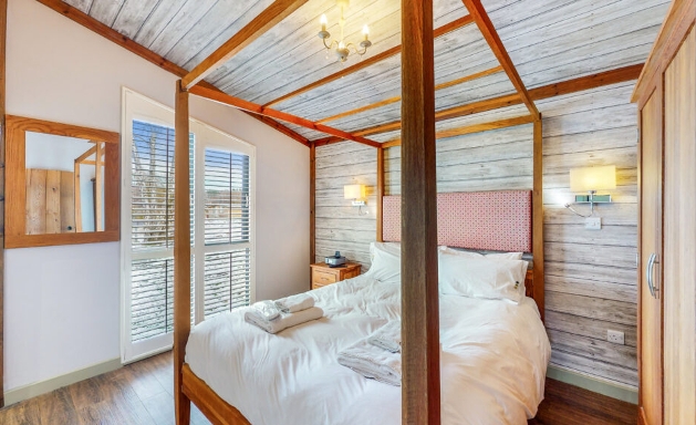 four-poster wooden bed in a room with panelled walls and ceiling and wood floor