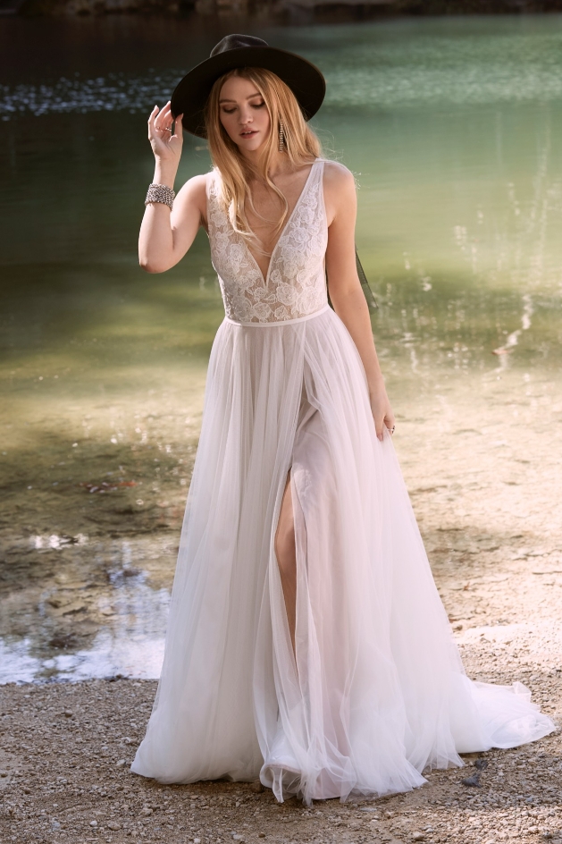 bride by a lake wearing flowing dress with black hat