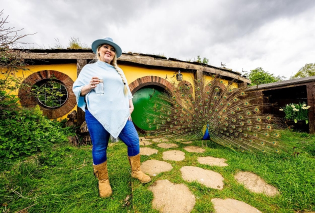 Lady in hat standing next to hobbit hole