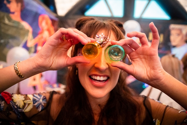 part goer with shot glasses held up to her eyes in colourful attire