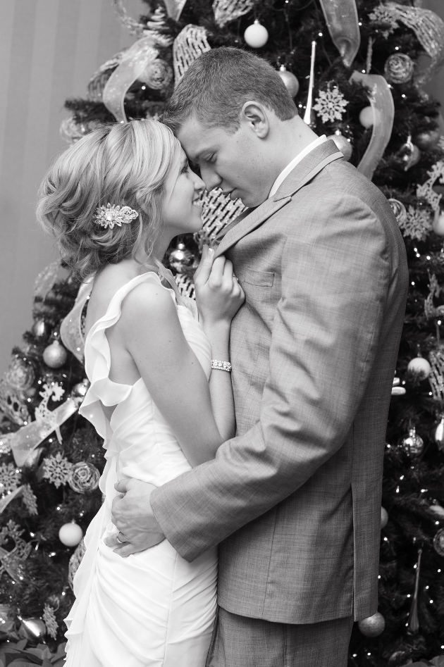 bride and groom embraced in front of a christmas tree