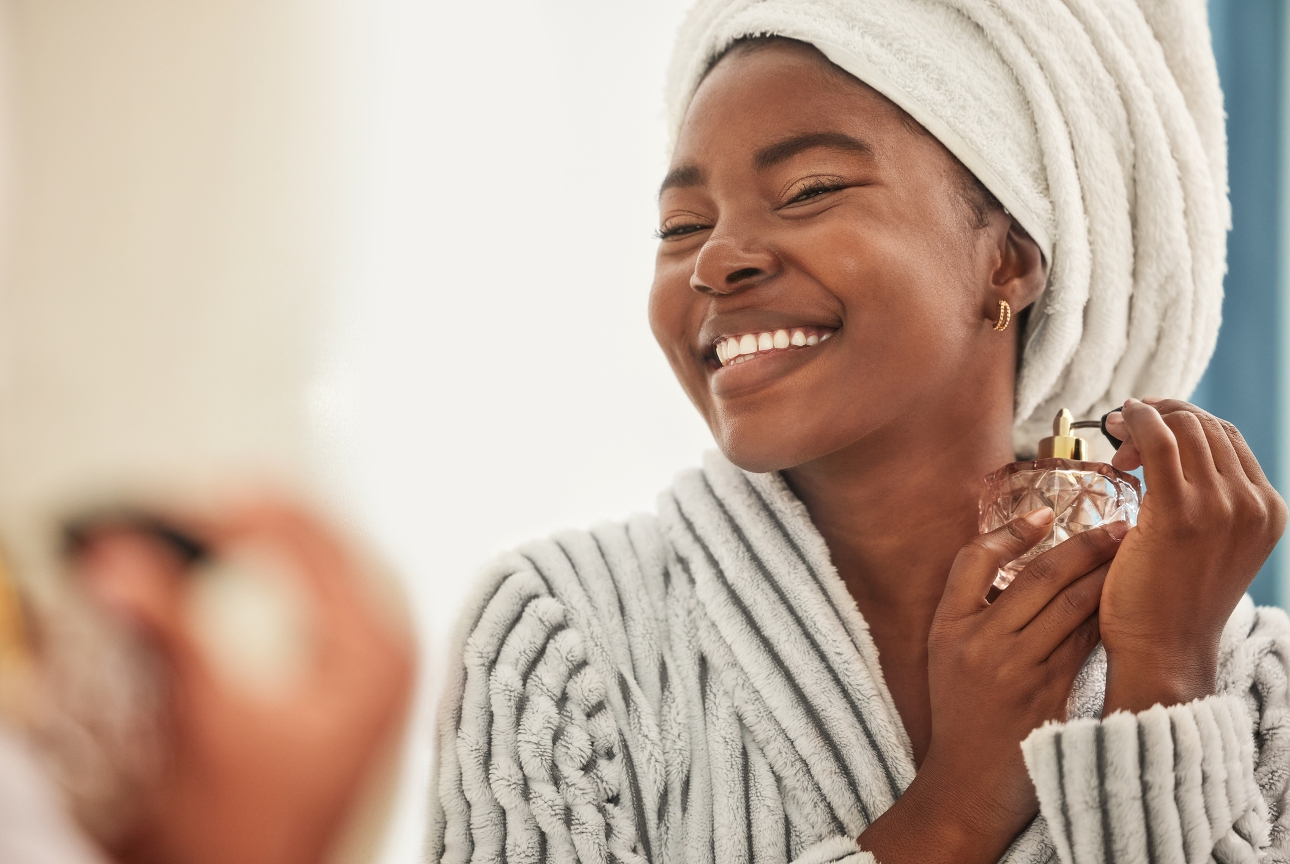 woman in robe and hair in a towel spraying perfume