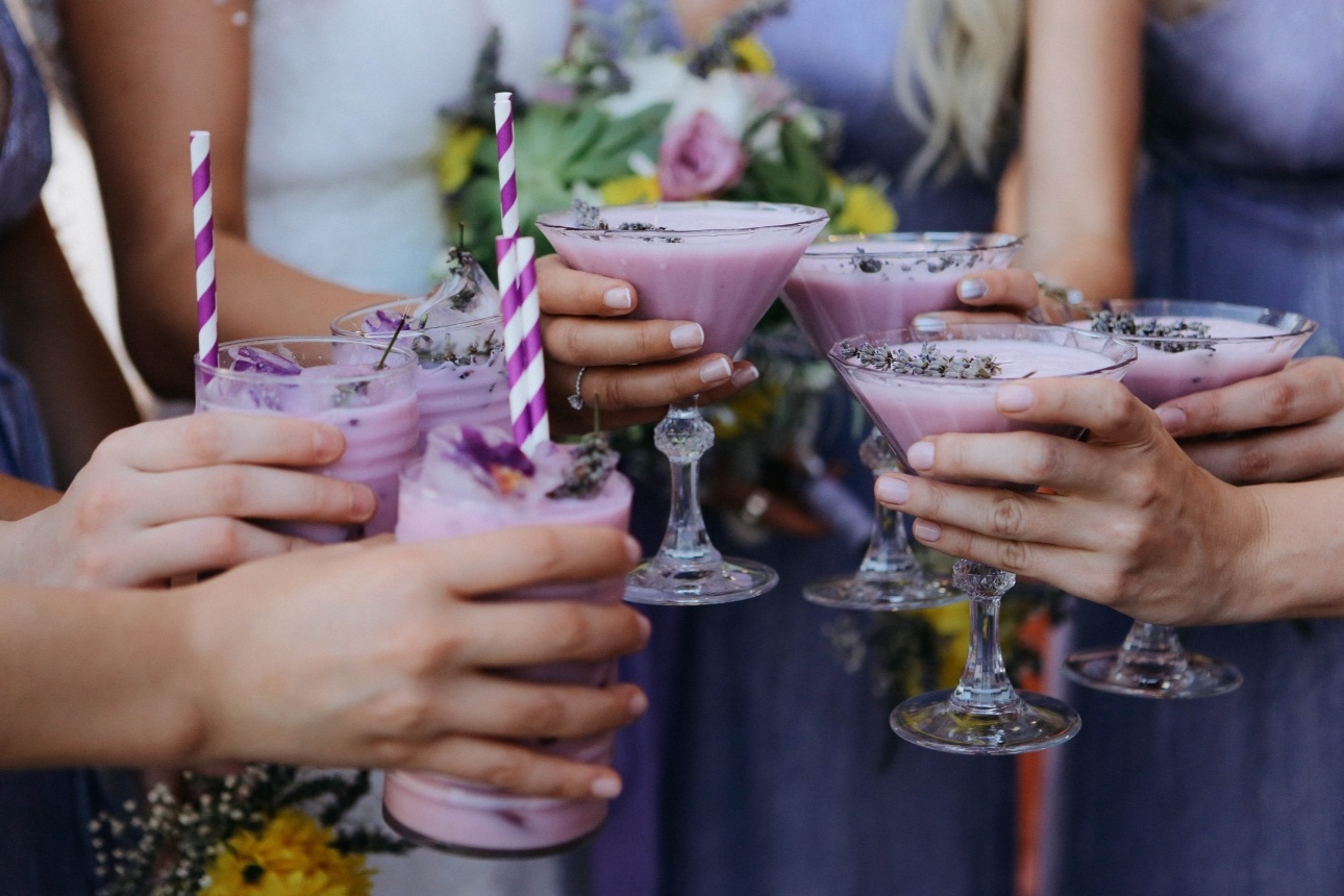 bride and bridesmaids holding cocktails that match the colour of their dresses: purple