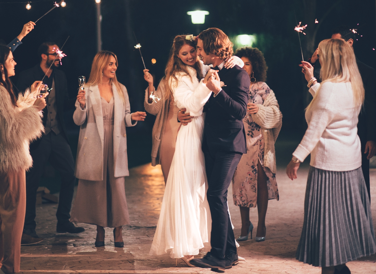 wedding couple dancing outside on their wedding day while guests wave sparklers