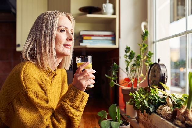 woman in yellow jumper drinking glass of water looking out the window