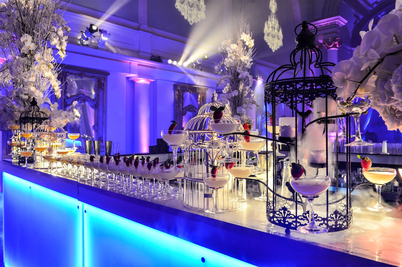 bar lit up with UV lights, flowers and display cages of drinks on bar