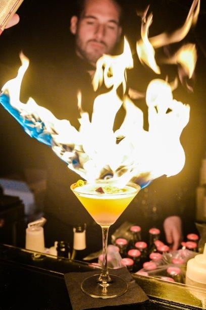 cocktail on fire with bar tend holding a firelight