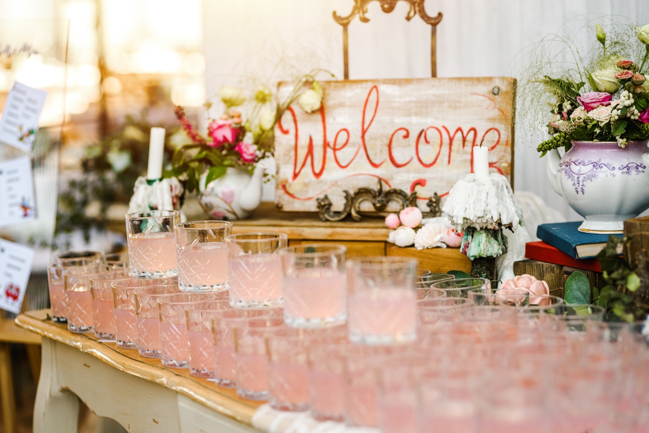 wedding cocktails lined up on a makeshift bar at wedding welcome sign in background