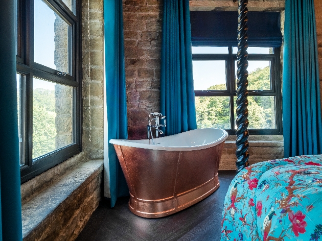 large copper free stand bath in room brick walls black window frames large blue bed