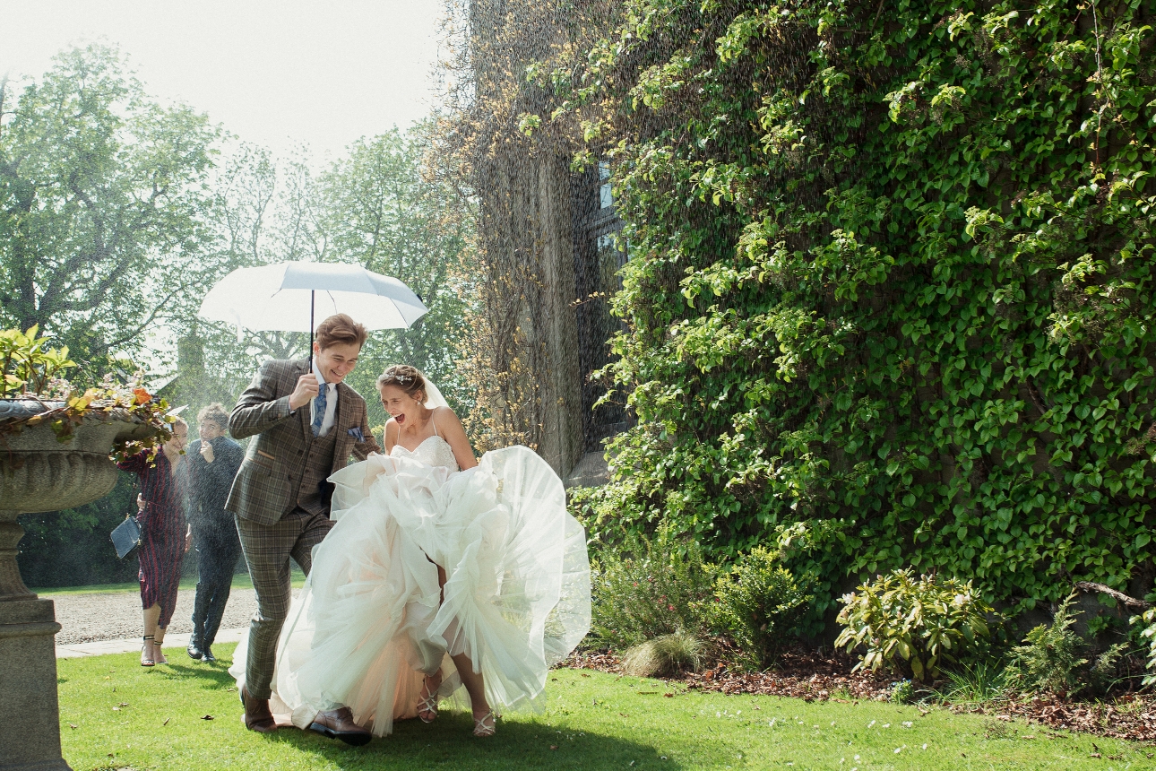 bride and groom on wedding day with umbrella getting caught in downpour