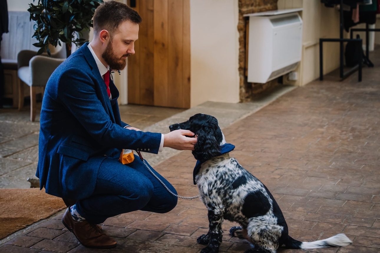 groom in blue suit bent down with his dog