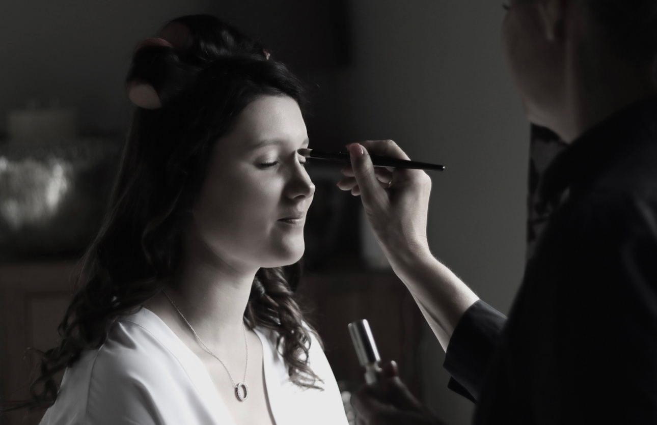 Black and white image of bride having her wedding make up applied by makeup artist