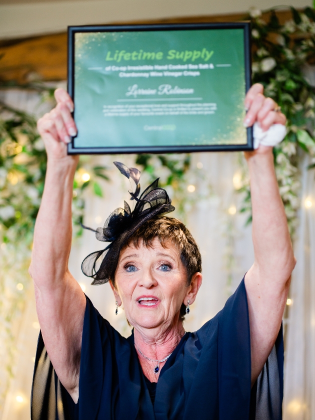 mother of the bride holds up lifetime supply of coop crisps certificate