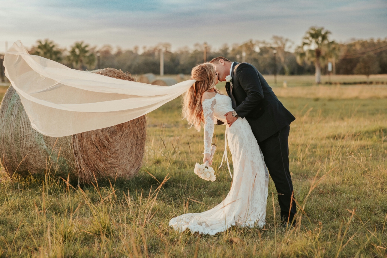 couple after their wedding in a field kissing veil in air